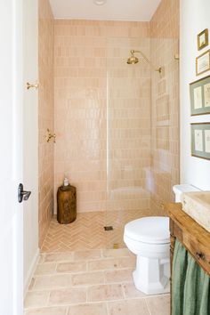 a white toilet sitting next to a walk in shower under a light pink tiled wall