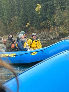 three people in a blue raft on the water with trees in the backgroud