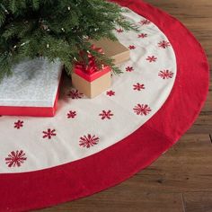 a christmas tree with presents under it on a red and white round tablecloth covered in snowflakes