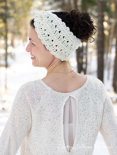 a woman wearing a white crochet headband in the snow with trees behind her