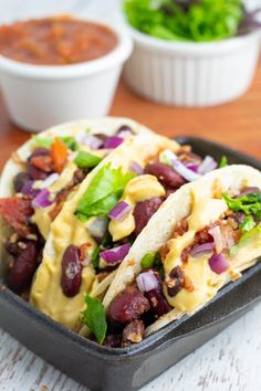 two tacos with beans, lettuce and cheese in a black tray on a table