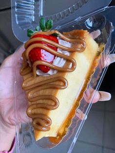 someone holding up a piece of cheesecake with chocolate sauce and strawberries on top