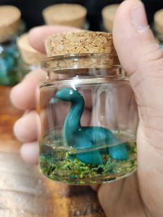 a hand holding a glass jar filled with small blue dinosaurs in it's mouth