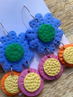 four colorful flower shaped earrings sitting on top of a piece of paper next to an envelope