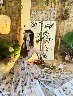 a woman sitting on the ground in front of a bamboo tree with her hands up