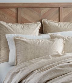 an unmade bed with white linens and pillows on top of it, in front of a wooden headboard