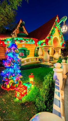 a christmas tree is lit up in front of a house with lights and decorations on it