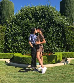 a man and woman kissing in front of hedges