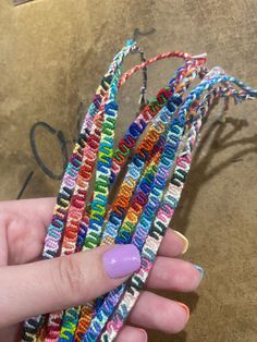 a woman's hand holding several multicolored seed beaded bracelets in her left hand