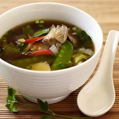 a white bowl filled with soup on top of a wooden table next to a spoon