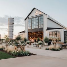 an outdoor venue with tables and chairs in the foreground, surrounded by tall silos