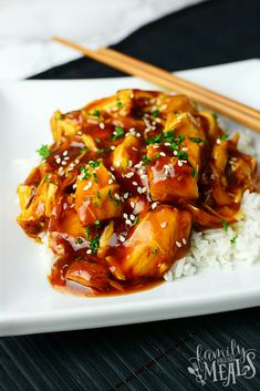 a white plate topped with chicken and rice next to chopsticks on a table