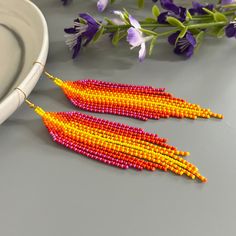 two pairs of beaded earrings sitting on top of a table next to purple flowers