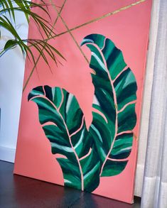 a painting of a large green leaf on a pink wall next to a potted plant