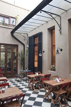 an outdoor patio with tables and chairs on checkered tile flooring in front of a building