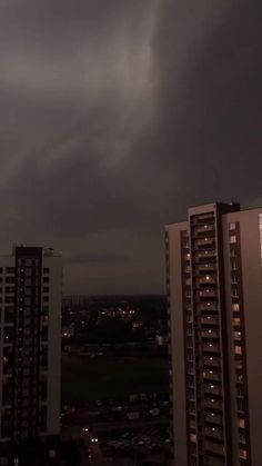 dark clouds loom over the city skyline at night with buildings lit up in the foreground