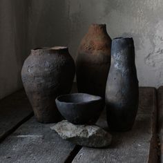 three vases sitting on top of a wooden table next to a bowl and rock