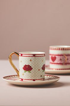 two cups and saucers with designs on them sitting on a table next to each other