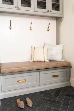 a bench with two pillows and some shoes on the floor next to it in front of a cabinet