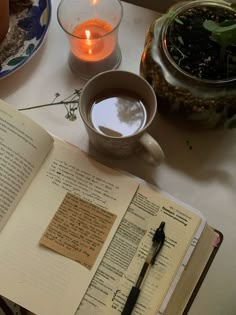 an open book sitting on top of a table next to a cup of coffee and a candle