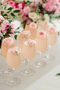 several glasses filled with champagne and pink flowers on a table next to vases full of white and pink flowers