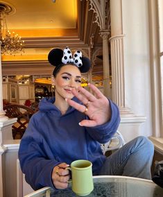 a woman sitting at a table with a coffee cup in front of her and mickey mouse ears on her head