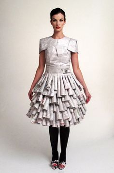 a woman standing in front of a white wall wearing a dress made out of newspapers