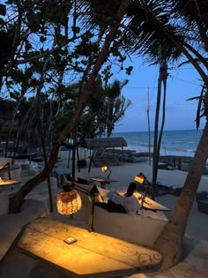 people are sitting at tables on the beach by the water with lights in their hands