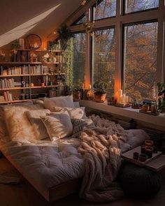 a bed sitting in front of two large windows next to a book shelf filled with books