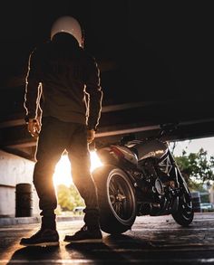 a person standing next to a motorcycle in the dark with sunlight coming through it's windows