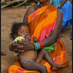 a woman holding a baby in her arms while sitting on the ground next to other people