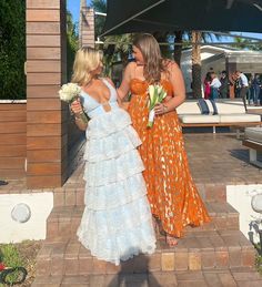 two women in dresses are walking down the sidewalk together and one is holding a bouquet