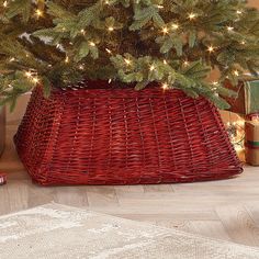 a christmas tree in a red basket on the floor with lights and presents under it