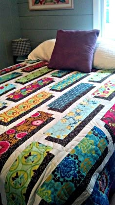 a bed with a colorful quilt on top of it next to a window in a room