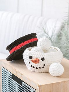 a crocheted snowman basket and hat sitting on top of a wooden table