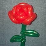 a red balloon flower sitting on top of a green stick in front of a gray wall