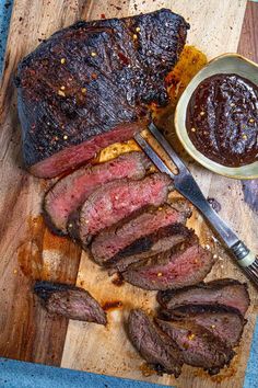 sliced steak on cutting board next to knife and bowl of bbq sauce with fork