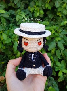 a small crocheted doll wearing a black suit and white hat with red eyes