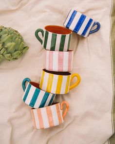 four striped mugs sitting on top of a bed next to an artichoke