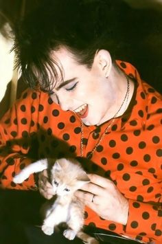 a woman in an orange polka dot shirt holding a kitten with her mouth wide open