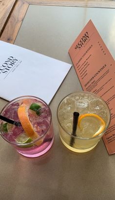 two cocktails are sitting on a table next to a menu