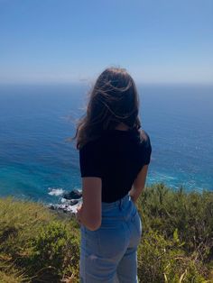 a woman standing on top of a lush green hillside next to the ocean