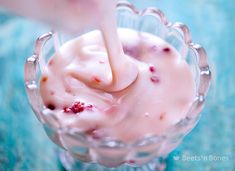 a person is dipping something into a small glass bowl filled with ice cream and cranberries