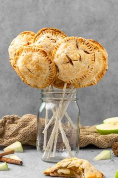 apple pies in a glass jar with apples around it and cinnamon sticks sticking out of the top