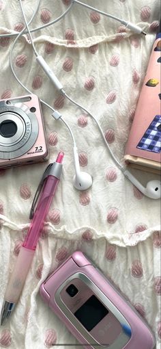 two cell phones, a pen and ear buds laying on a bed next to each other