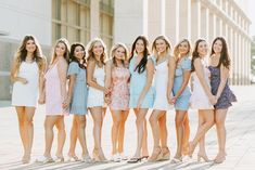 a group of young women standing next to each other in dresses and sandals on the sidewalk