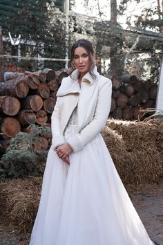 a woman in a white dress and coat posing for the camera with logs behind her