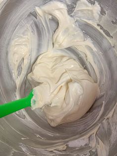 a mixing bowl filled with whipped cream and a green spatula