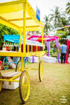 a yellow cart with drinks on it sitting in the grass