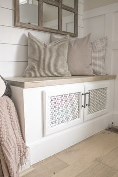 a white bench with pillows on top of it and a mirror over the back wall